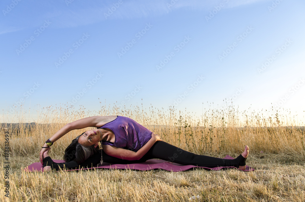 Young woman in yoga stretch, on yoga mat, outdoors. Beautiful scenery, dry grass and sunset . Copy space Young woman in yoga stretch, on yoga mat, outdoors. Beautiful scenery, dry grass and sunset . Copy space