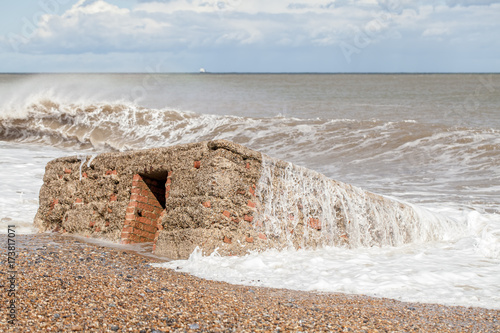 WW2 military anti-invasion beach structure. Historical concrete coastal defense building claimed by the sea. photo