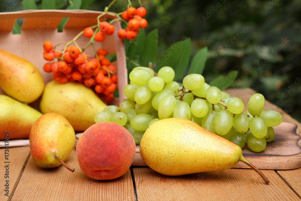 Pears, peach, green grapes, rowan berries in a wooden box on a wooden table in the woods at the time of harvesting Pears, peach, green grapes, rowan berries in a wooden box on a wooden table in the woods at the time of harvesting