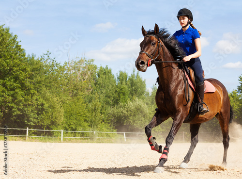 Female jockey galloping on horseback at racetrack