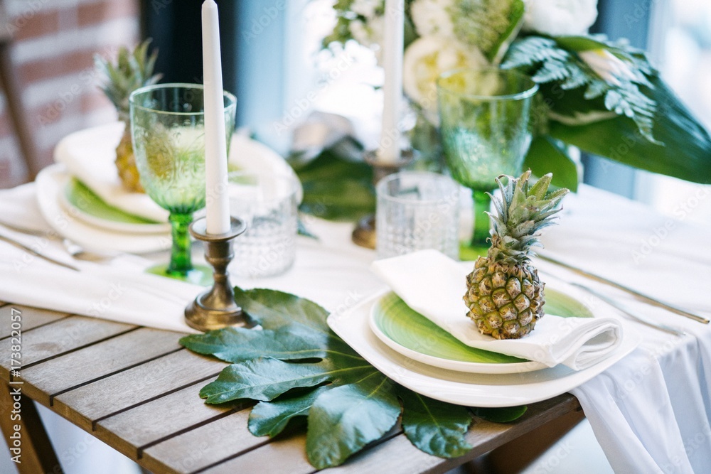 plates on the table decorated with pineapples, candles and flowers, green and white colour