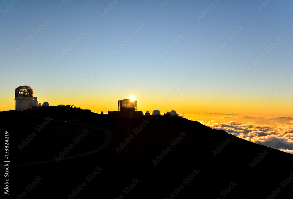Spectacular sunset on the summit of Haleakala mountain (10,023 ft), the highest volcano on the island of Maui, Hawaii. Astronomy observatories in the background. Famous tourist destination.