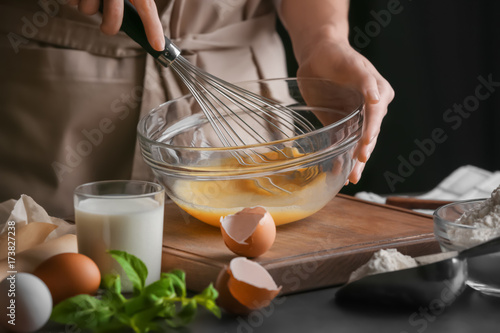 Female chef whisking eggs in glass bowl on kitchen table photo