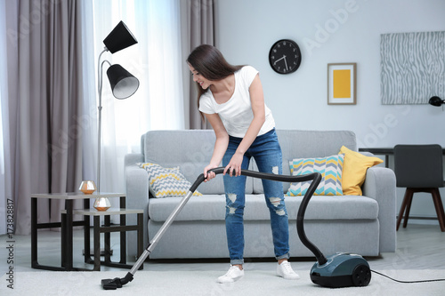 Woman cleaning carpet with vacuum in living room photo