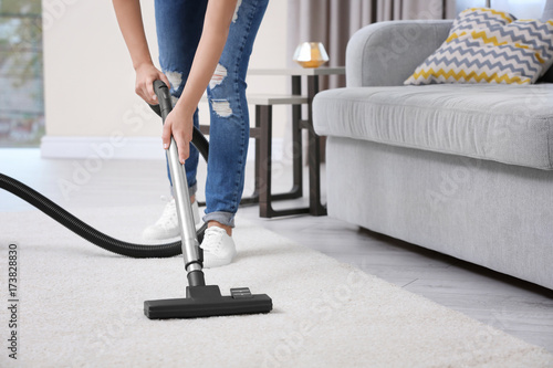 Fotografie Woman cleaning carpet with vacuum in living room