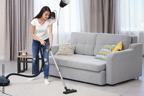 Woman cleaning carpet with vacuum in living room