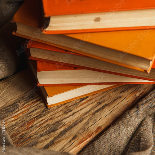 A stack of paper books in orange color on textured wooden surface. Autumn mood concept. Time to read.