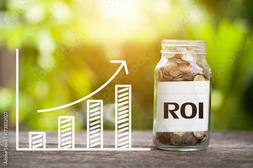 ROI (Return on Investment) Word With Coin In Glass Jar and graph up. Online advertising Concept photo