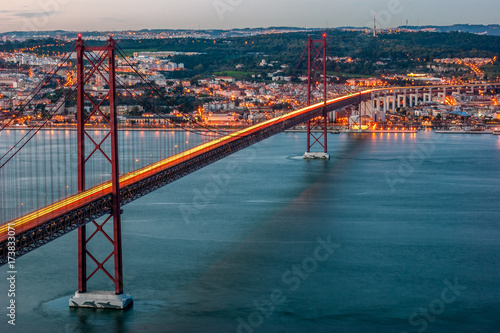 Sunset over the ' 25 April ' bridge with reflection of the lights of the cars in the road, in Lisbon, capital of Portugal