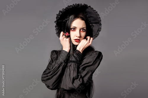 Portrait of brunette woman in black dress and classic gothic style with red eyes on gray background. halloween concept. photo