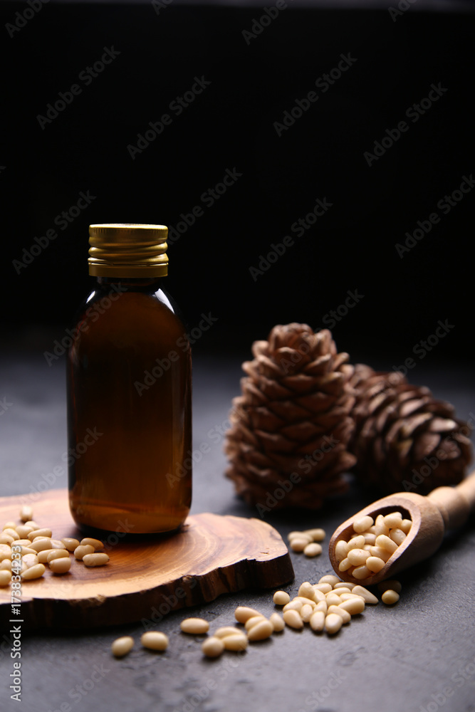 Essential cedar oil in glass bottle with raw nuts and cones on dark background with copy space Essential cedar oil in glass bottle with raw nuts and cones on dark background with copy space