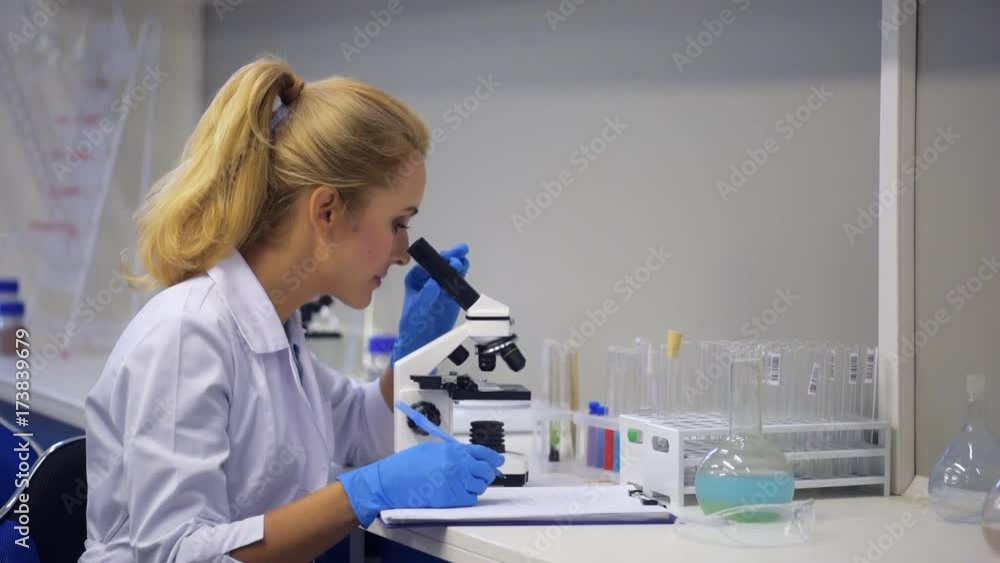 Science professional smiling for camera while looking through microscope Science professional smiling for camera while looking through microscope