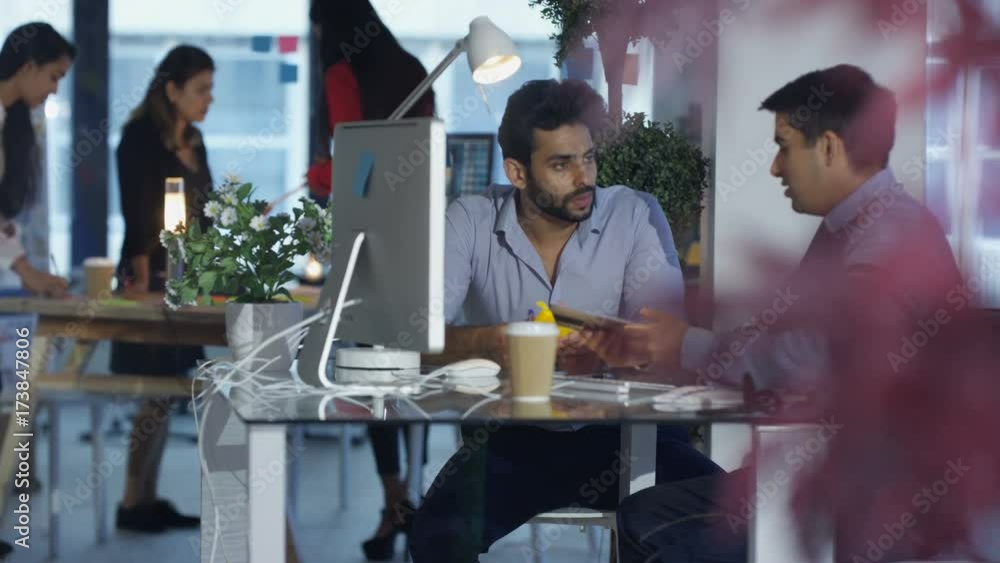 Designers at desk with colleagues working in background. Designers at desk with colleagues working in background.