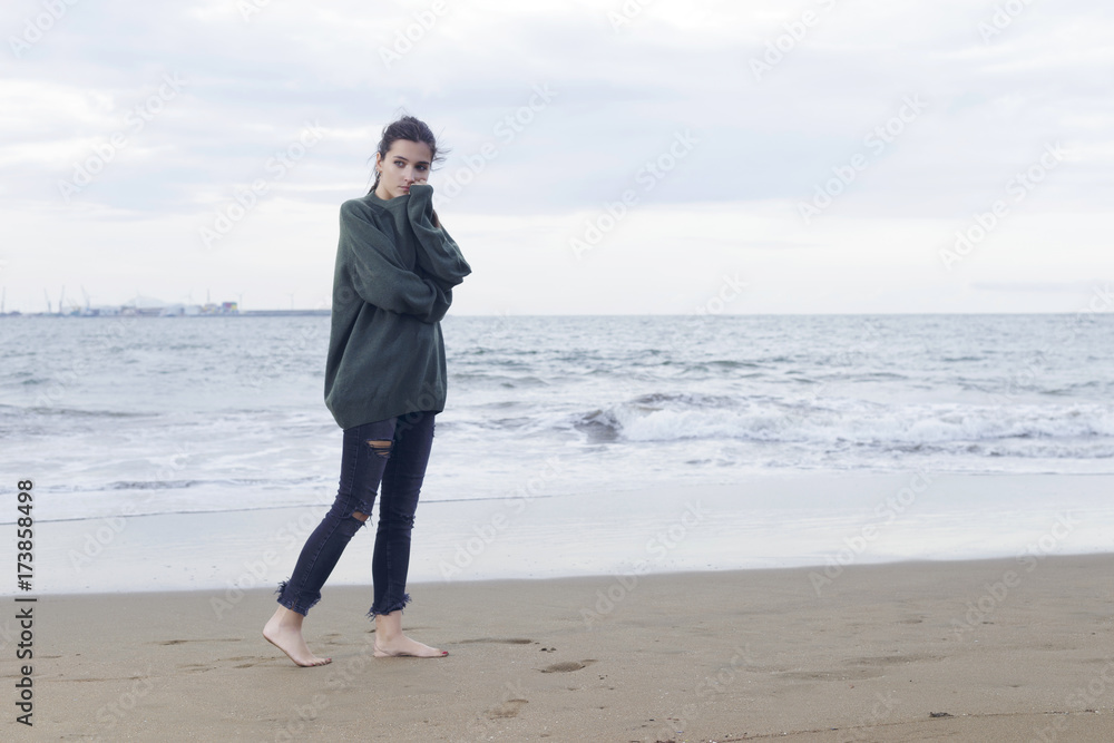 Young pretty woman standing alone on the beach near the sea, waiting for somebody in the ocean. Young pretty woman standing alone on the beach near the sea, waiting for somebody in the ocean.