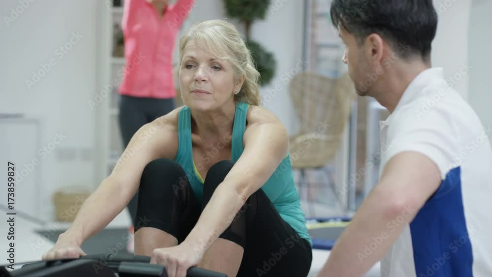 Mature woman working out on rowing machine with personal trainer Mature woman working out on rowing machine with personal trainer
