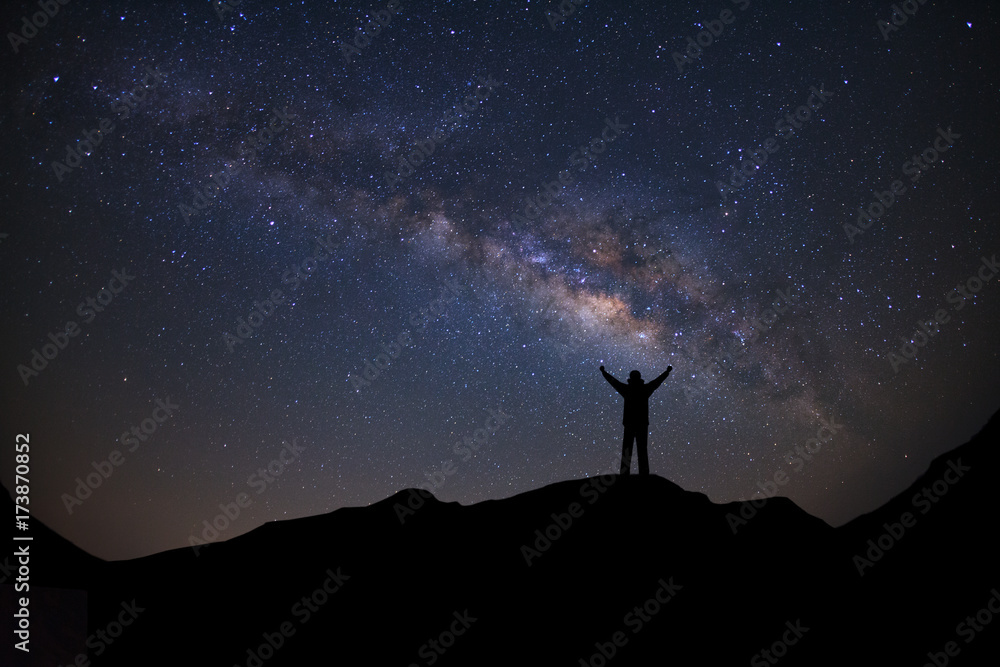 Panorama landscape with milky way, Night sky with stars and silhouette of a standing sporty man with raised up arms on high mountain.
