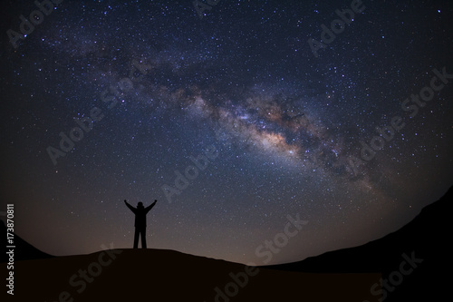 Panorama landscape with milky way  Night sky with stars and silhouette of a standing sporty man with raised up arms on high mountain.