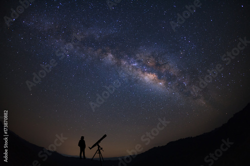 Silhouette of a standing man with telescope watching the wilky way galaxy