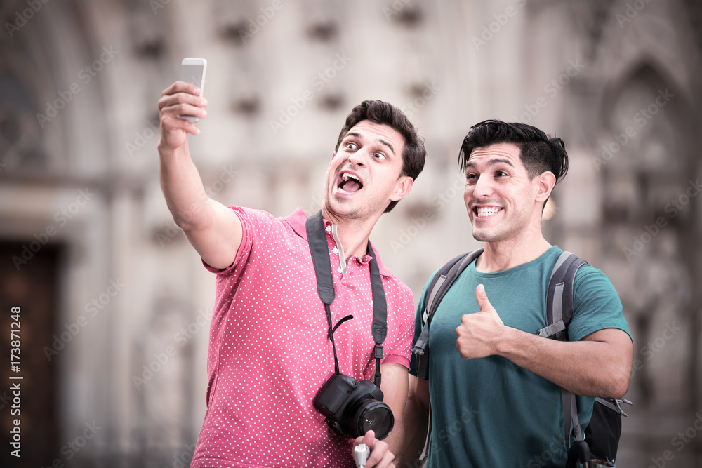 Fototapeta premium positive men tourists with suitcases are making selfie in unknown city