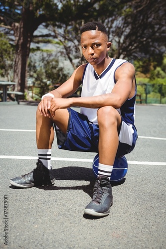 Portrait of male teenager sitting on basketball © wavebreak3