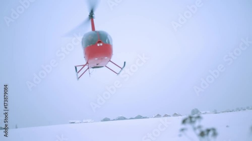 A red helicopter is flying over the field. Shooting from the ground.