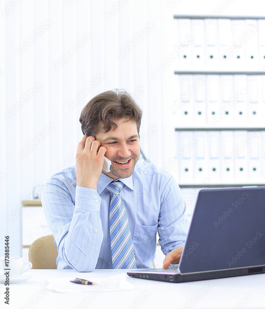 handsome businessman sitting at Desk and talking on a cell phone handsome businessman sitting at Desk and talking on a cell phone