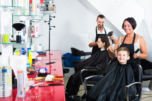 Boy sitting in barber salon and getting hairstyle