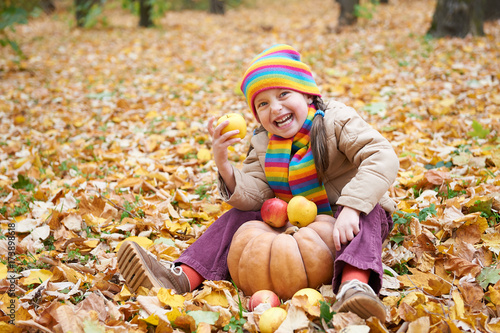 child having fun with apple and pumpkin in forest  sit on autumn leaves background  fall season