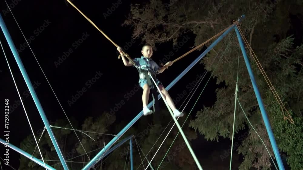 Scarred Little boy playing bungee jumping trampoline outside at dark Scarred Little boy playing bungee jumping trampoline outside at dark