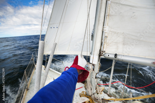 View of a yacht in strong wind with a sailors hand holding a cable in a glove photo