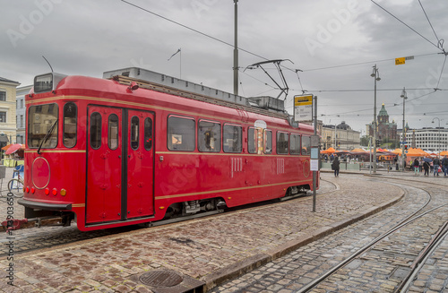 A beautiful vintage red tram used as a pub at the stop Kauppatori Salutorget, in the historic center of Helsinki, Finland, with the Dormition Cathedral (Uspenskin katedraali) in the background