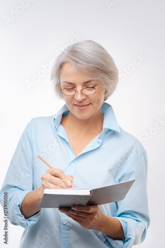 Beautiful grey-haired woman writing in notebook