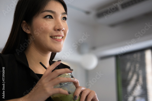 portrait of young asian businesswoman hold green tea cup at coffee shop. asian woman smile   relax in cafe.