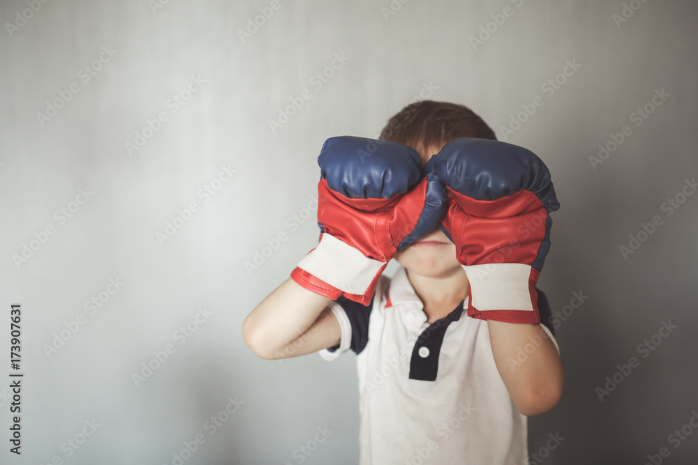 Kid boy in boxing gloves on neutral at home