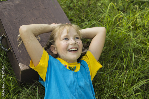 a fair-haired, freckled girl, lies on the grass, she has a suitcase under her head, she dreams of traveling.