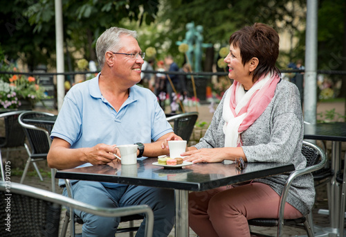 Senior couple in love sitting in street cafe, drinking coffee, talking, laughing and having fun. Happy people in retirement concept.