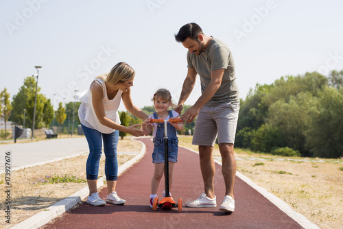 Young parents teaching daughter to ride a scooter for the first time