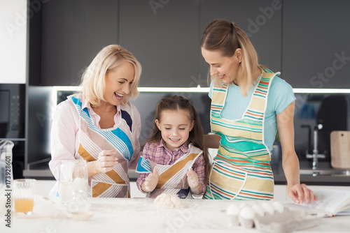 A girl, her mom and grandmother prepare a homemade cake. They knead the dough