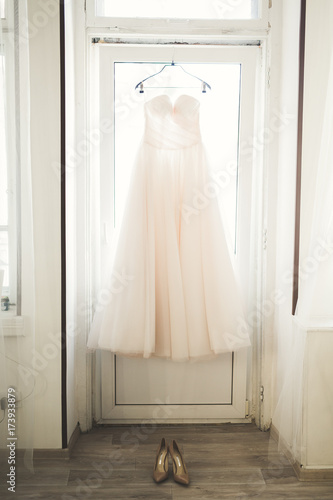 Fashion wedding dress for bride hanging near window