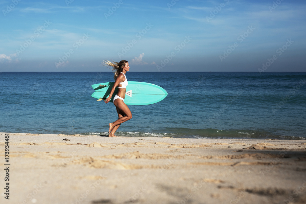 Beautiful young woman in bikini with surf board at beach of tropical island.