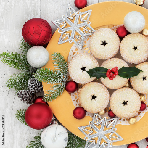 Christmas mince pies on a gold plate with holly, fir, bauble decorations on rustic wood background