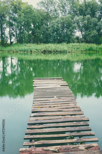 Pier on a calm river in the summer. Wooden pier bridge in the morning. Place for fishing in the river. Toned, style photo.