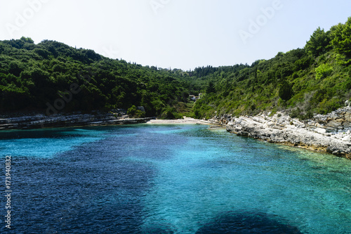 Scenic View Of Vibrantly Coloured Ionian Sea Surrounded By Forest And Cliffs Against Clear Sky