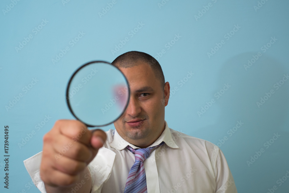 Businessman in a suit looks through a magnifying glass Businessman in a suit looks through a magnifying glass