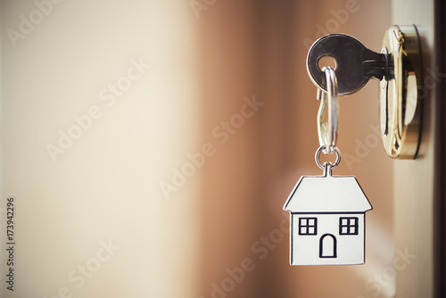 House key on a house shaped silver keyring in the lock of a door