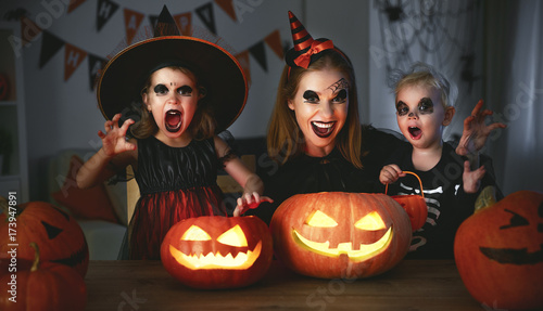 family mother and children in costumes and makeup to halloween with pumpkin in   dark