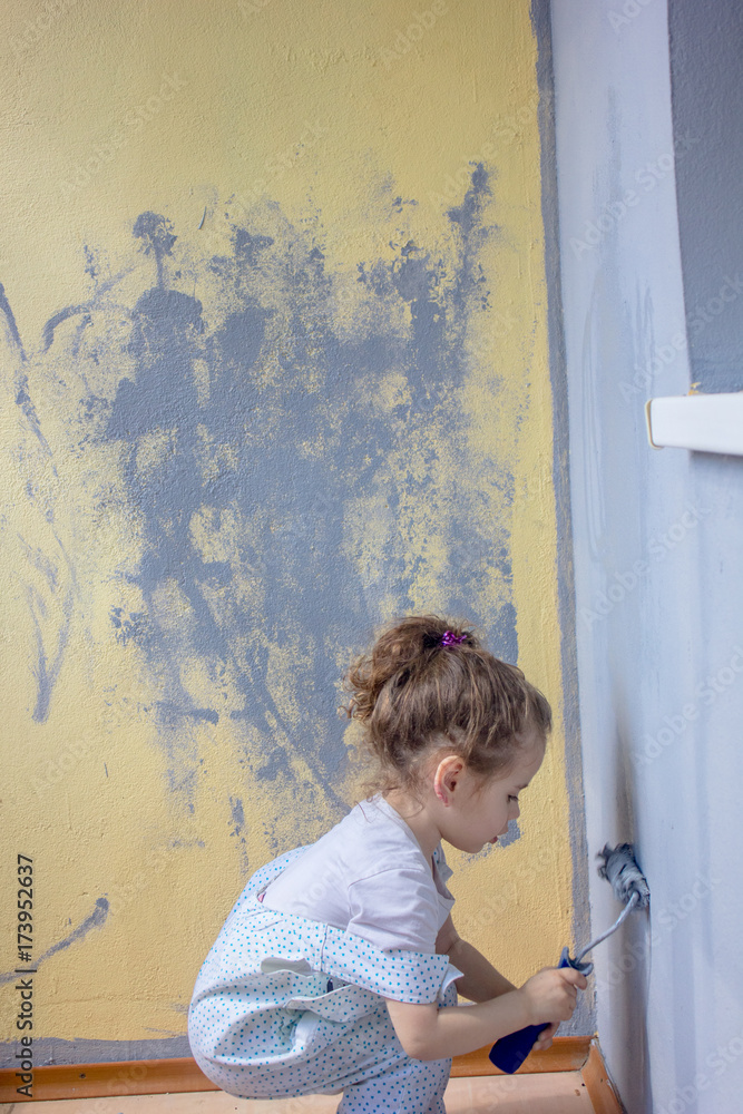 Naklejka premium Little kid girl paints wall by paint roller