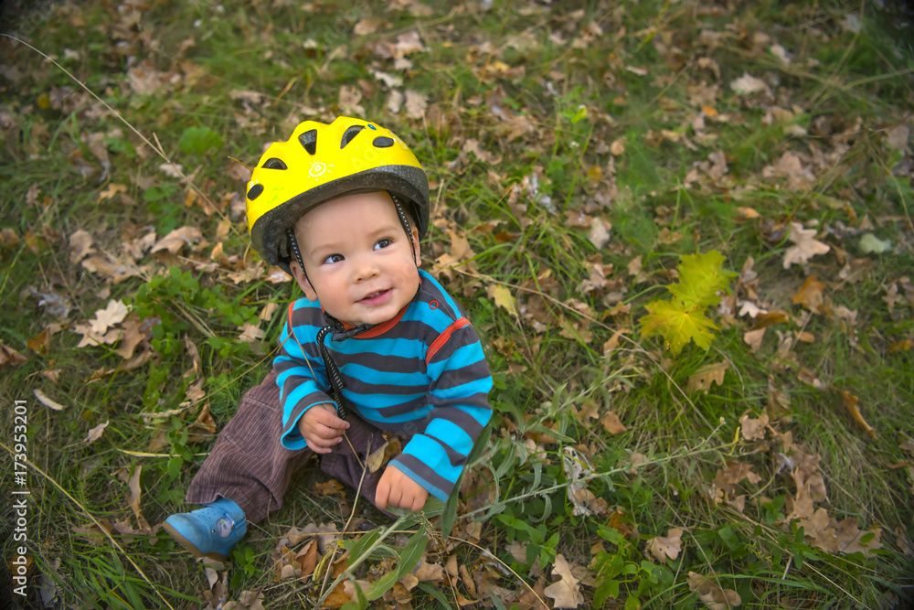Cute baby boy with safety helmet sitting in the autumn park