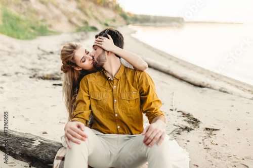 A lovers is kissing. Young couple is having fun and hugging on the beach. Beautiful girl embrace her boyfriend from back. Wedding walk. A newlyweds looks at each other. Artwork