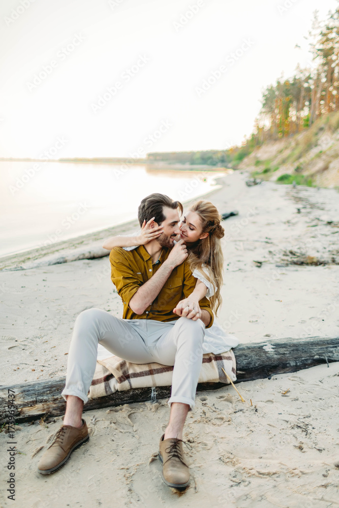 A young couple is hugging on the beach. Beautiful girl embrace her boyfriend from back. Wedding walk. A newlyweds looks at each other. Artwork A young couple is hugging on the beach. Beautiful girl embrace her boyfriend from back. Wedding walk. A newlyweds looks at each other. Artwork
